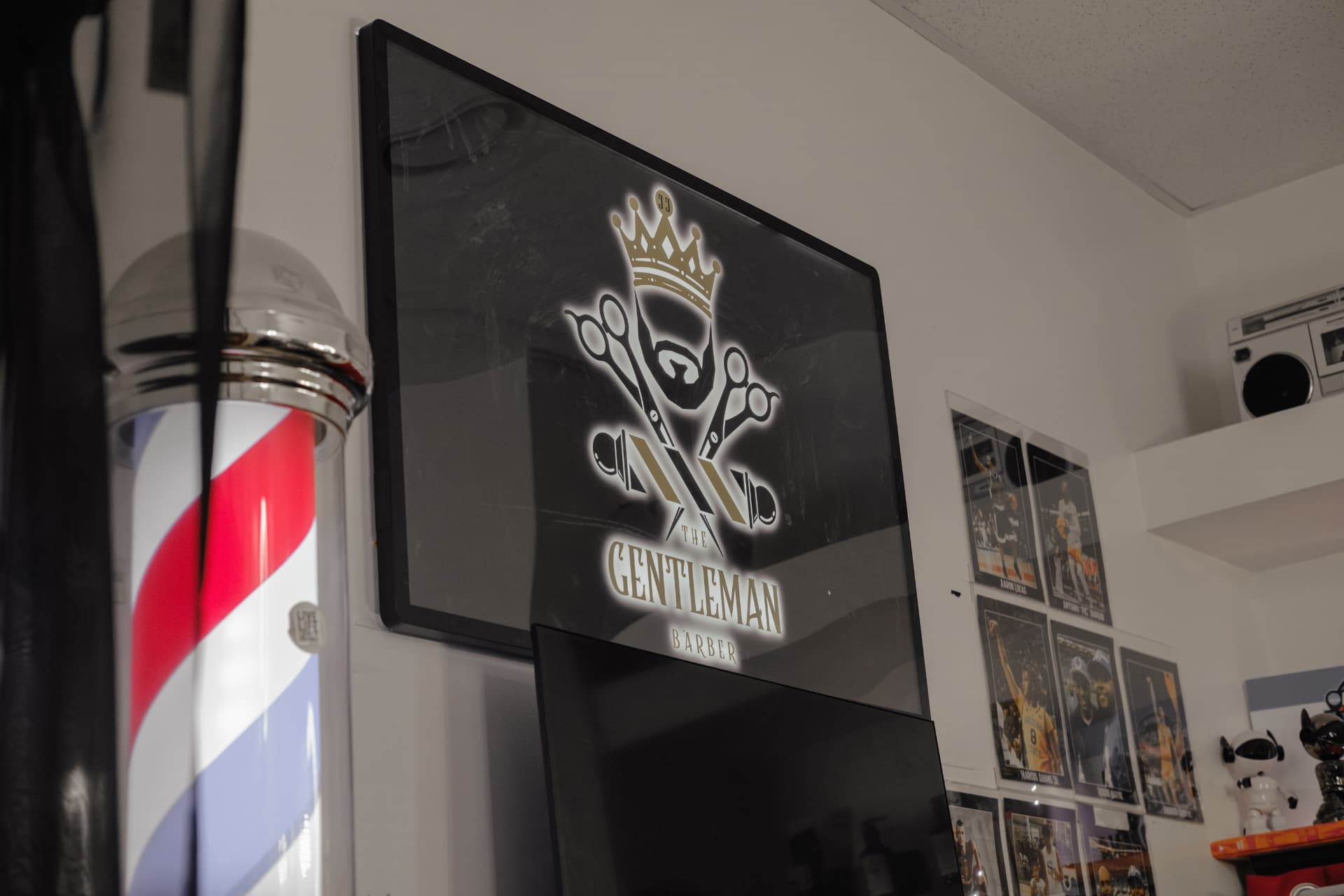 A framed The Gentleman Barber shop sign on the wall next to a barber pole